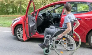 Uomo in carrozzina accanto a un'auto rossa con portiera aperta. Un disabile può avere due auto intestate per maggiore autonomia.