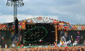 Ogromna scena festiwalowa z napisem "Poland Rock" i kolorowymi grafikami. Tłum ludzi czeka na koncert.