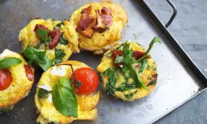 Matiga muffins med ägg, spenat, tomat och bacon på en plåt. Perfekt för en mättande frukost eller brunch.