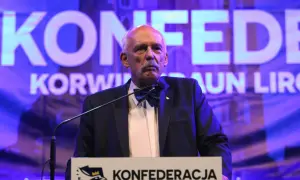Mężczyzna w garniturze i muszce przemawia na tle napisu "KONFEDERACJA".