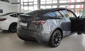 Szary Tesla Model Y z otwartymi drzwiami, obok biały Model 3. Wymiary tego SUV-a są idealne do miasta i na dalsze trasy.