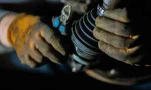 Mechanik w rękawicach naprawia przegub w samochodzie, używając szczypiec.
