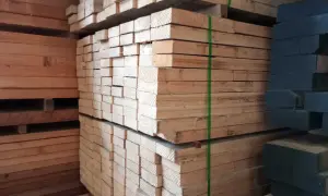 Piles of light-colored lumber, possibly madera ayous, are stacked high. A stack of dark wood is visible on the right.