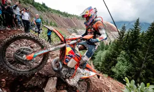 Motocyklista walczy z kamienistym podjazdem podczas Erzberg Rodeo. Widzowie obserwują zmagania na stromym zboczu.