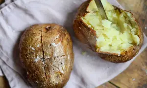 Perfekt bakad potatis i airfryer, en är uppskuren och visar det fluffiga inkråmet. Saltkorn glittrar på den gyllene ytan.