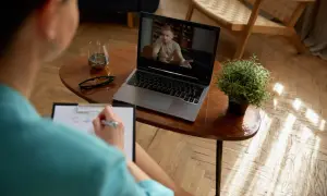 Kobieta prowadzi psychoterapię przez Skype, notując na bieżąco. Na ekranie laptopa widać mężczyznę w gabinecie.