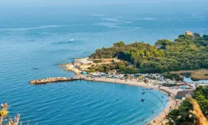 Una splendida spiaggia delle Marche, con un molo affollato, stabilimenti balneari e una pineta lussureggiante che si estende fino al mare.