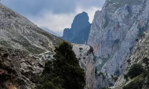 Majestuosas montañas y un camino serpenteante en la ruta del Cares, bajo un cielo nublado que presagia lluvia.