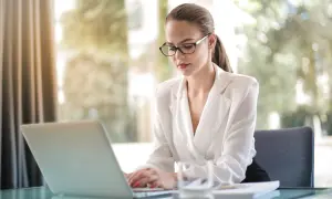 Kobieta w okularach pracuje na laptopie, planując swoją działalność nierejestrowaną.