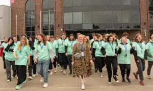 Grupa młodych ludzi w zielonych koszulkach z napisem "Szkoła w chmurze" idzie przed budynkiem.