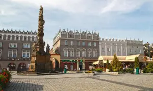 Rynek w Raciborzu z zabytkową kolumną i kamienicami. W tle apteka i kawiarnie z ogródkami.