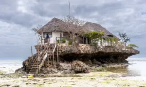 Wyjątkowy dom na skale, idealne miejsce na zanzibar wakacje. Drewniane schody prowadzą do restauracji z trawiastym dachem.