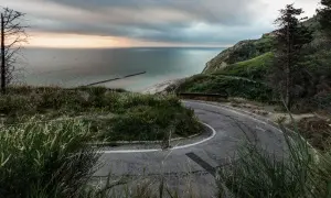 Strada tortuosa nel parco naturale regionale del Monte San Bartolo, con vista sul mare Adriatico e una spiaggia sabbiosa.
