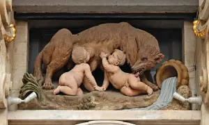 Rzeźba przedstawia wilczycę karmiącą Romulusa i Remusa, symbolizującą legendę o założeniu Rzymu. To klasyczny przykład motywu salut rzymski.