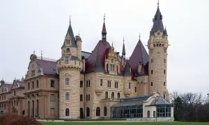 Zamek Książ, jeden z najpiękniejszych zamków w Polsce, z charakterystycznymi wieżami i czerwonymi dachami, otoczony zielenią.