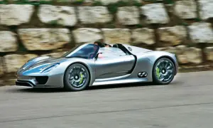 Srebrny Porsche 918 Spyder pędzi po drodze, z kierowcą za kierownicą.