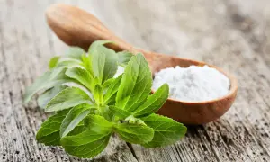Foglie verdi di stevia accanto a un cucchiaio di polvere bianca. Alcuni si chiedono se la stevia fa male.