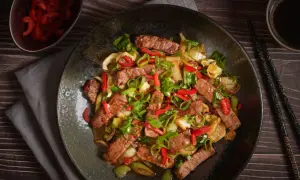 Pyszne wieprzowina w sosie teriyaki z papryką i szczypiorkiem, podana na ciemnym talerzu.