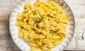 Piatto di pasta e zucca cremosa, guarnita con prezzemolo tritato e pepe nero, servita su un piatto bianco con bordo decorato.