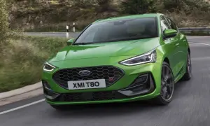 Jaskrawozielony Ford Focus 2025 ST z charakterystycznym grillem i światłami LED pokonuje zakręt na malowniczej, leśnej drodze.