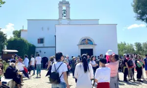 Folla di fedeli davanti alla chiesa di Santa Maria di Merino, con il campanile e un mosaico sopra l'ingresso.