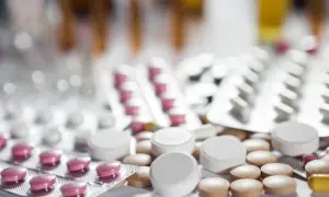 Zbliżenie na opakowania leków i tabletki, w tym różowe tabletki w blistrze i białe tabletki luzem. Może to być lek pramolan 50 mg.