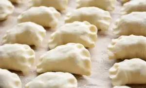 Gotowe do gotowania ciasto na pierogi ułożone rzędami na blacie.