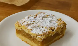 Kawałek babcinej szarlotki najlepszej, posypanej cukrem pudrem, na białym talerzyku.