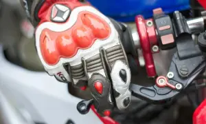 Dłoń w rękawicy motocyklowej trzymająca manetkę gazu i dźwignię sprzęgła.