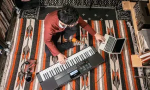Mężczyzna gra na keyboardzie Casio, obok laptop i słuchawki.