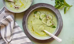 Deux bols de soupe froide aux concombres et menthe, arrosés d'huile d'olive et saupoudrés d'épices.