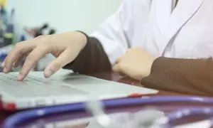 Lekarz wpisuje dane pacjenta na laptopie, co oznacza skierowanie na cito. Stetoskop leży obok.