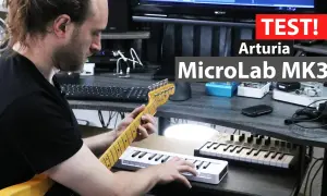 Mężczyzna gra na gitarze, obok niego leży biały midi keyboard Arturia MicroLab MK3.