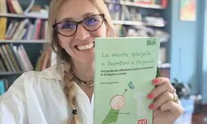 Donna sorridente con libro "La morte spiegata a bambini e ragazzi", affronta la paura di morire e lasciare i figli.