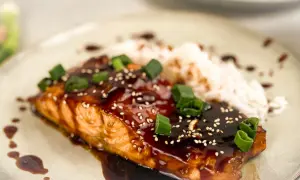 En saftig asiatisk lax med glansig teriyakisås, toppad med sesamfrön och salladslök, serveras med ris.