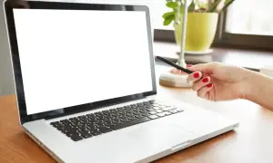 Dłoń z czerwonymi paznokciami wskazuje na biały ekran laptopa.