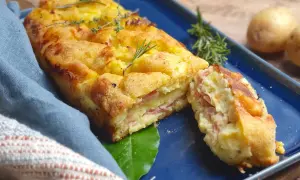 Polpettone di patate dorato e invitante, con strati di prosciutto e formaggio, guarnito con rosmarino e timo.