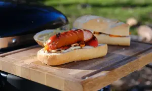 Pyszna kiełbasa z grilla w bułce z warzywami, gotowa do jedzenia na desce.