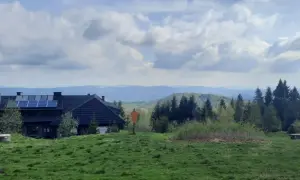 Dom z panelami słonecznymi na tle gór i lasów. Widok na szlaki Jaworzyny Krynickiej.