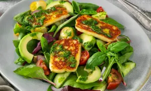 Pyszna sałatka z halloumi, awokado, pomidorkami i ogórkiem, polana zielonym sosem.