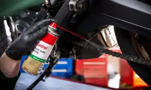 Ręka w czarnej rękawiczce rozpyla smar Castrol na łańcuch motocykla.