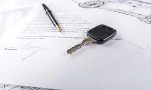 Kluczyk do samochodu i długopis leżą na dokumencie, który wygląda jak umowa kupna sprzedaży samochodu.