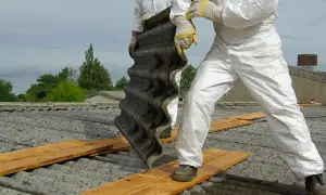 Arbeiter in Schutzanzügen entfernen eine Wellplatte. Bis in die 1990er Jahre wurde Asbest verbaut.