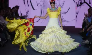Modelo desfila en la pasarela We Love Flamenco con un vestido blanco de lunares amarillos y volantes, portando un mantón amarillo con flores rojas.