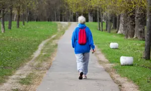 Spacer z plecakiem pod górę spala kalorie. Kobieta w niebieskiej bluzie i z czerwonym plecakiem idzie ścieżką w parku.