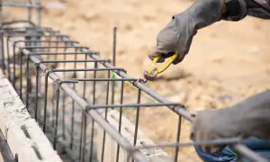 Manos enguantadas atando varillas de acero para como hacer los cimientos de una casa.