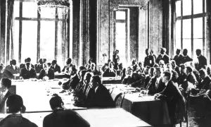 Männer in Anzügen sitzen an einem langen Tisch in einem prunkvollen Saal. Die Szene erinnert an die Unterzeichnung des **Versailler Vertrags**.