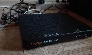 Czarny router Orange FunBox 2.0 z wieloma kablami podłączonymi do listwy zasilającej.