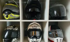 Sześć kasków motocyklowych różnych marek i stylów, ułożonych w białych przegrodach.