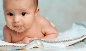 En bebis ligger på mage och det rinner saliv ur munnen. Bebis spyr mycket och det syns bubblor.